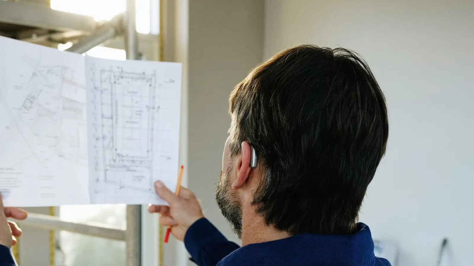 Estimator holding up a floor plan inside a house under renovation