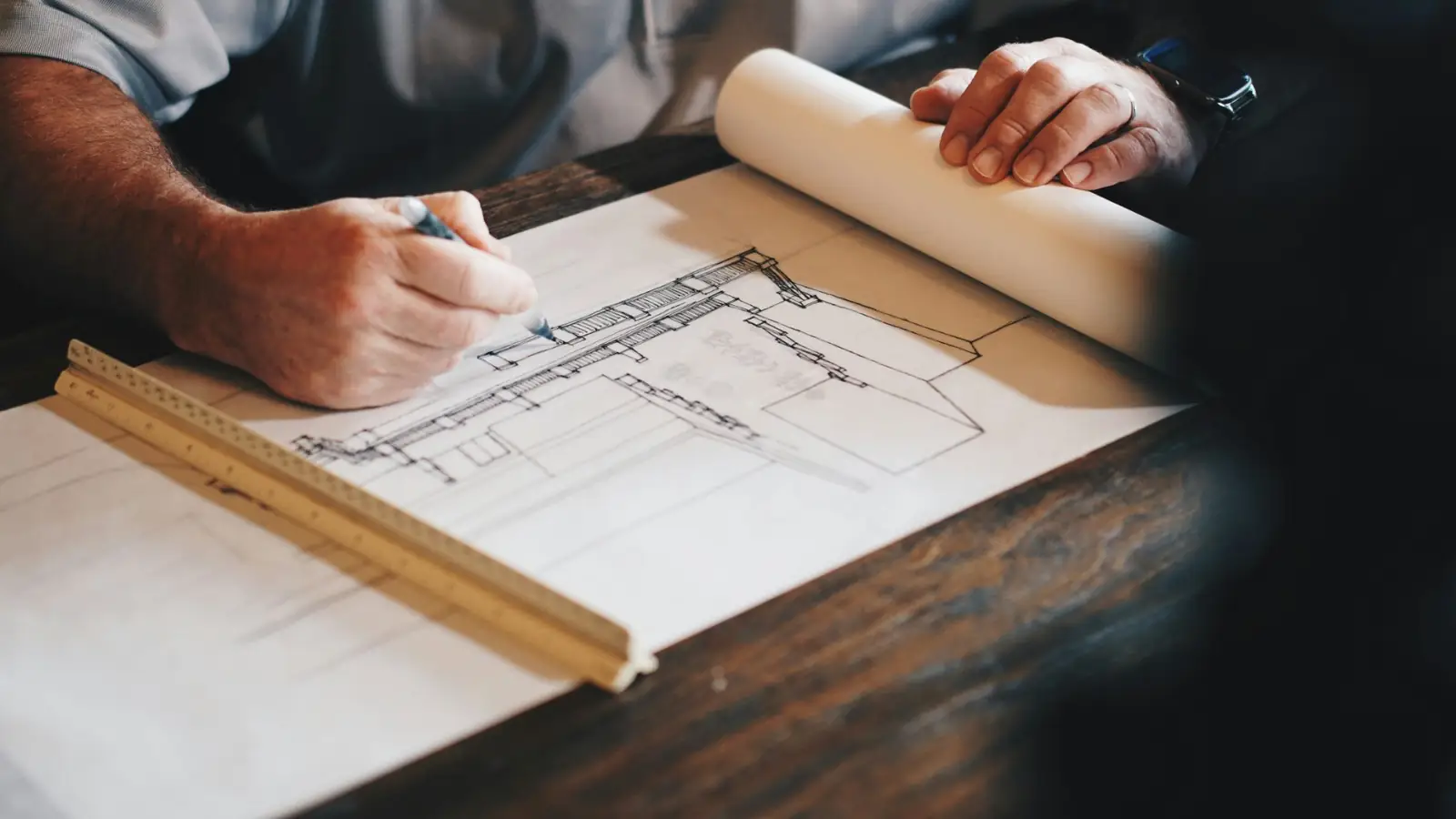 Estimator sketching a building section on drawing paper with a scale ruler